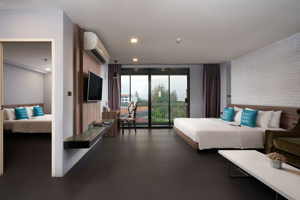 A modern hotel room with a bed, a sofa, a TV, a desk, and a balcony with a view.