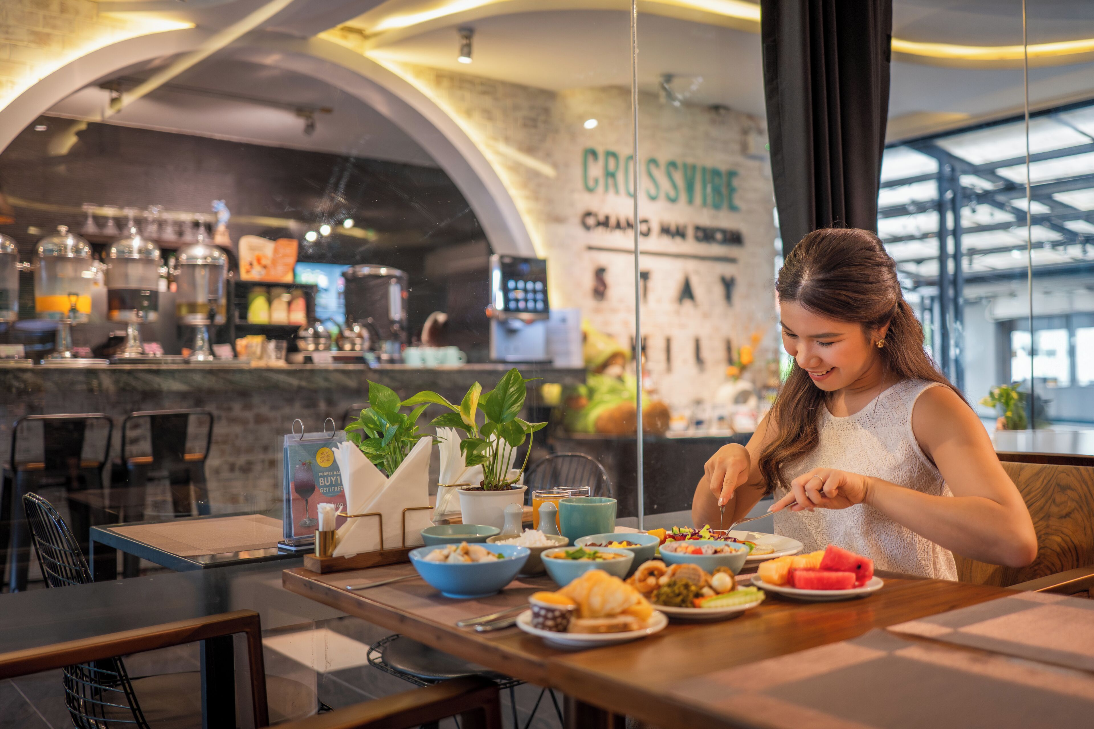 A person dining at a table with various dishes, a bar area in the background, and a sign that reads 'CROSSVIEW'.
