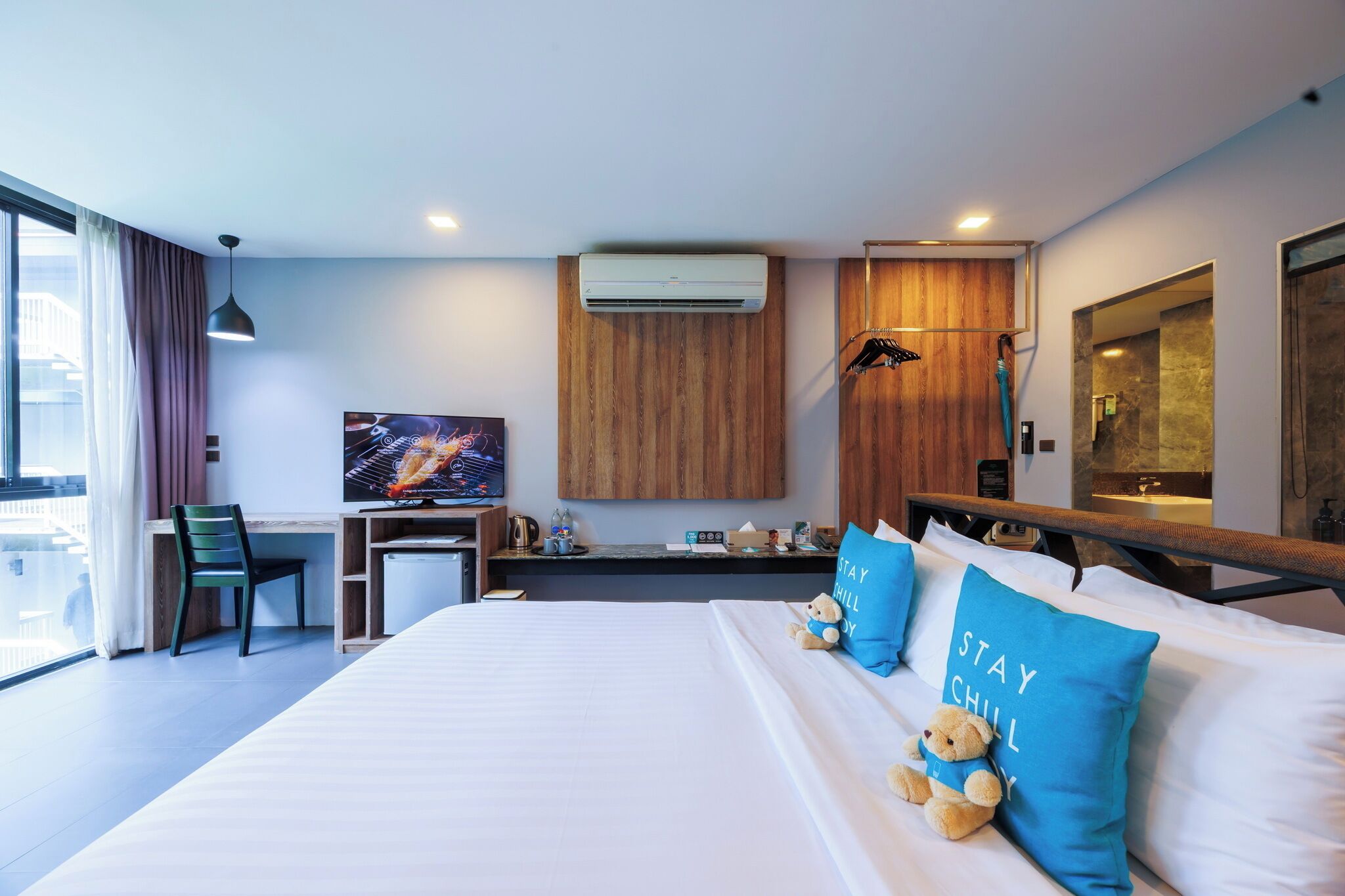 A hotel room with a bed, a desk, a TV, an air conditioner, a shower, and a large window.
