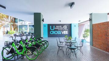 Una estación de alquiler de bicicletas con un letrero que dice 'U HAVE ARRIVED @ CROSS VIBE' y un área de estar con sillas y mesas.