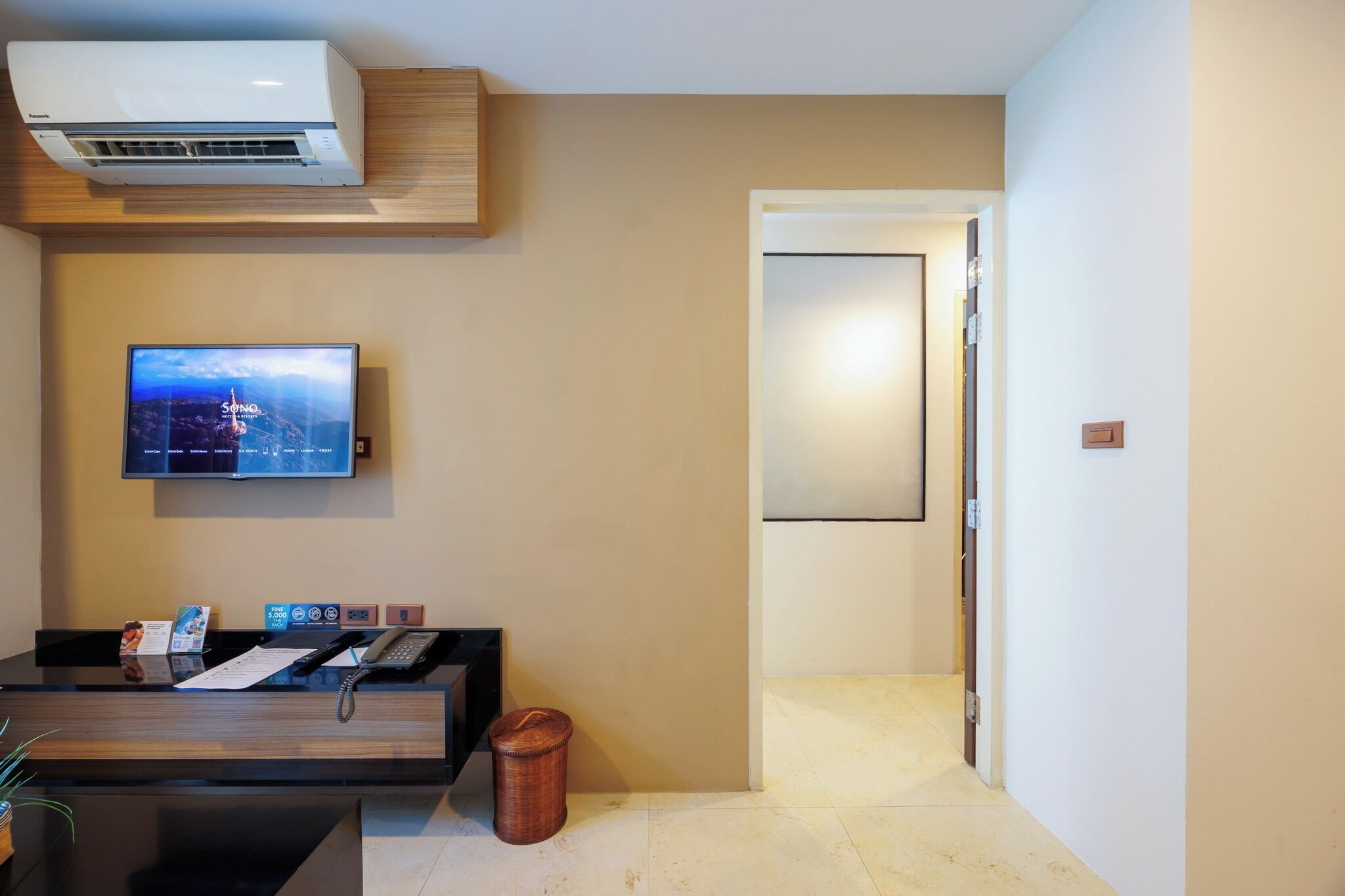 A hotel reception area with a flat-screen TV, a reception desk, a telephone, and an air conditioning unit.