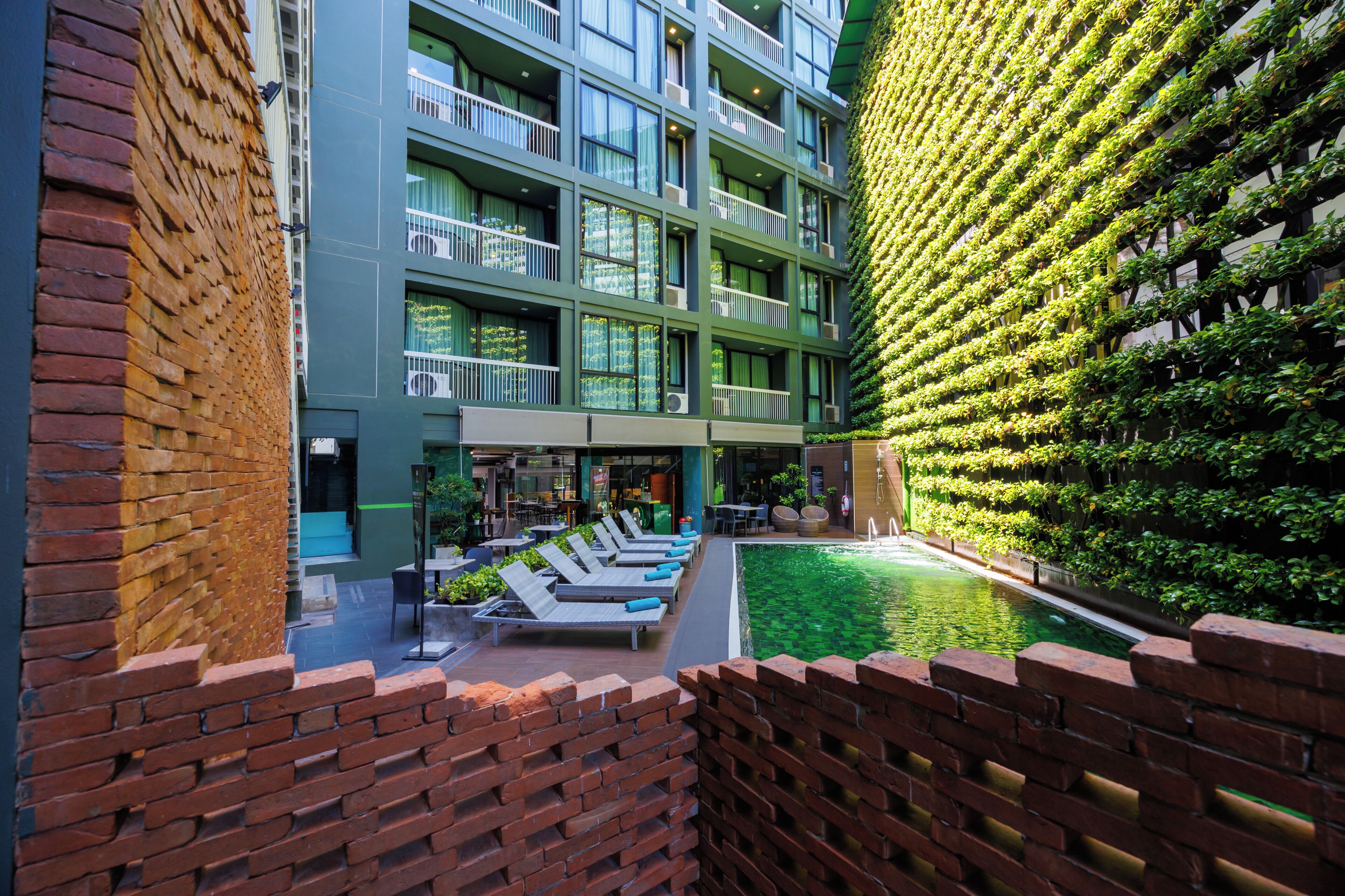 A hotel courtyard with a swimming pool, lounge chairs, and a green wall with plants.