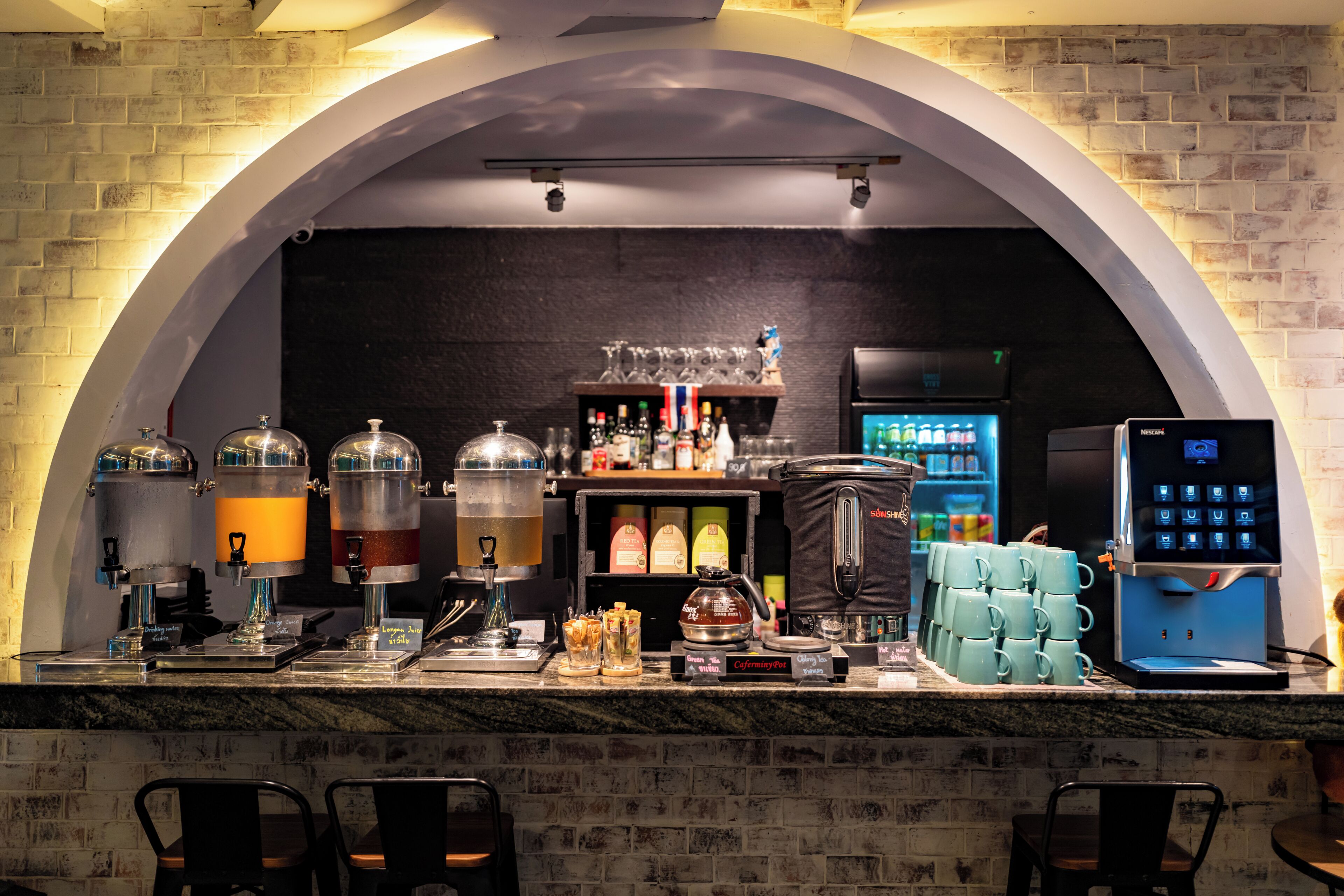 Un espace bar avec un mur en briques, une machine à café, un coin pour préparer le thé et un réfrigérateur.