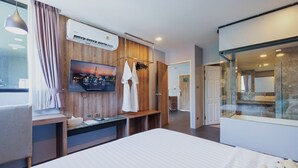 A modern hotel room with a bed, a TV, a wooden panel wall, a window with curtains, a desk, and a glass shower enclosure. - Cross Vibe Chiang Mai Decem (Chiang Mai)