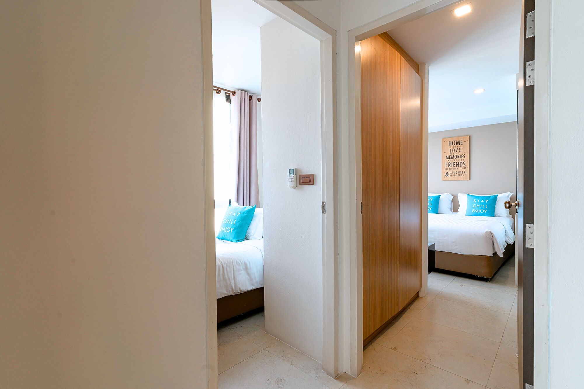 A hotel room with two beds, a wooden wardrobe, a wall-mounted light switch, and a motivational quote on the wall.