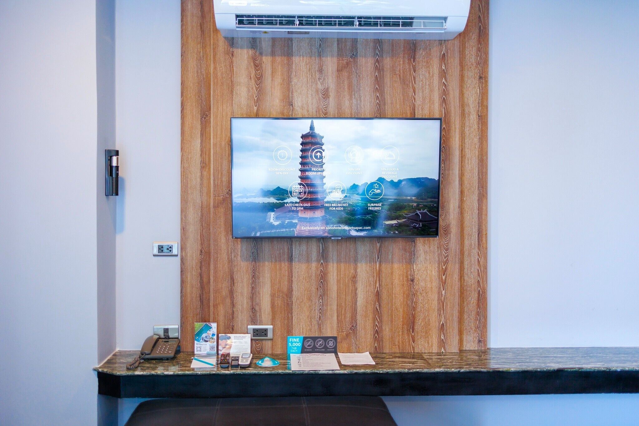 Un mostrador de recepción con un televisor mostrando una pagoda, un teléfono y folletos informativos.