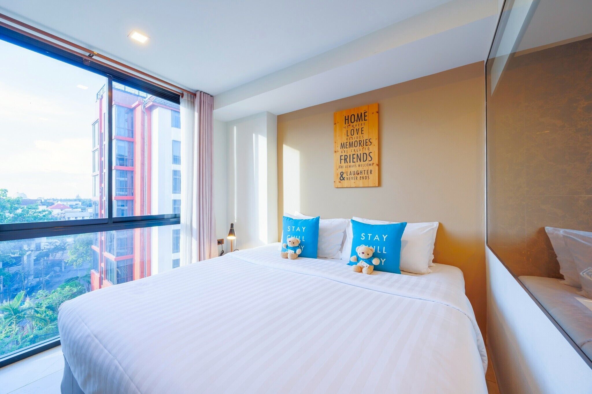 A hotel room with a large bed, a view of buildings, and a wall with a motivational quote.