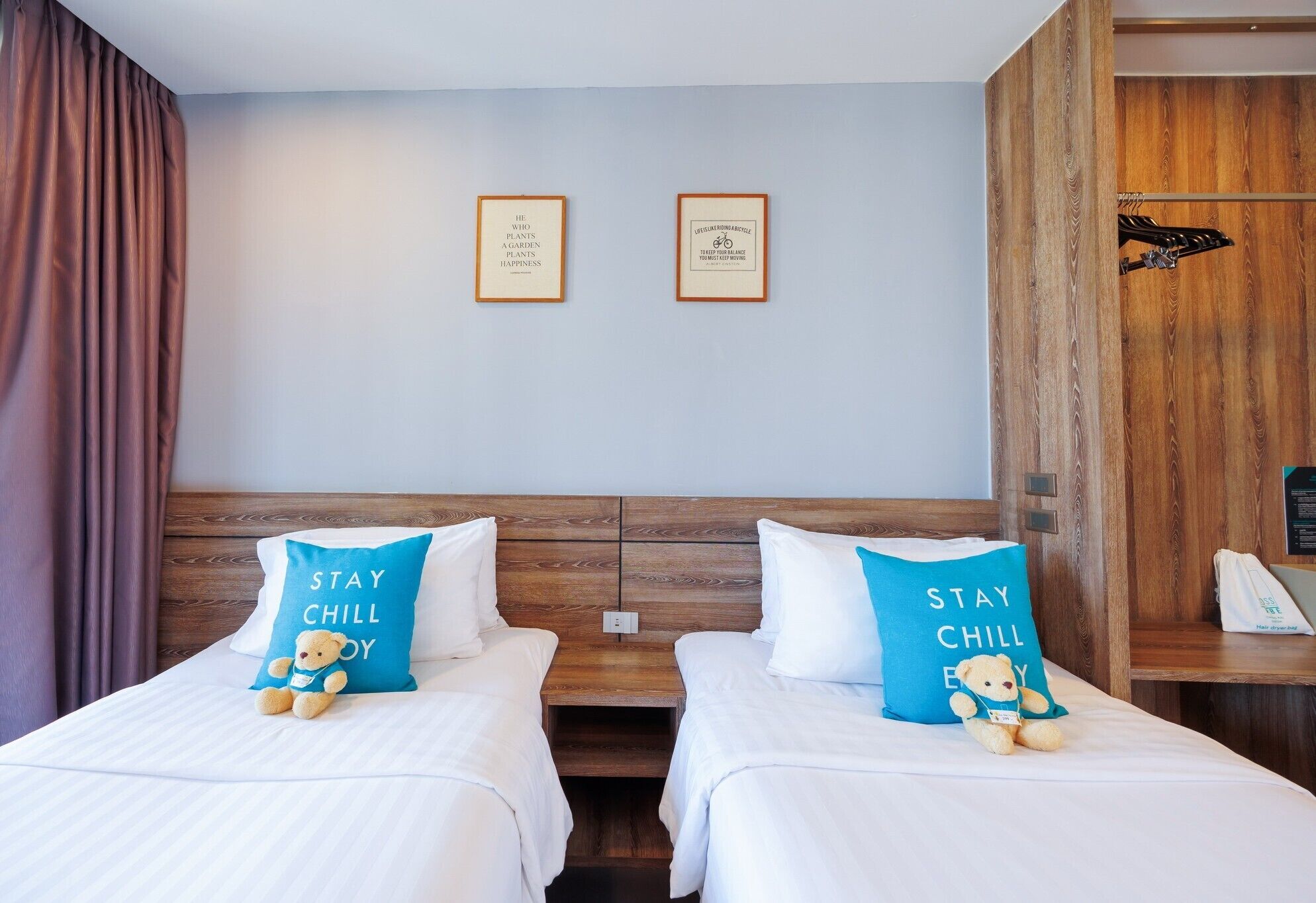 A hotel room with two beds, each with a pillow that says 'STAY CHILL'. There are two framed quotes on the wall above the beds.