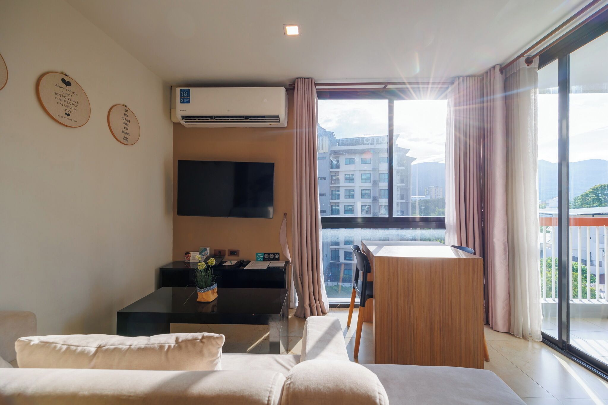 A modern living room with a sofa, a small table with a vase, a flat-screen TV, and a balcony with curtains.