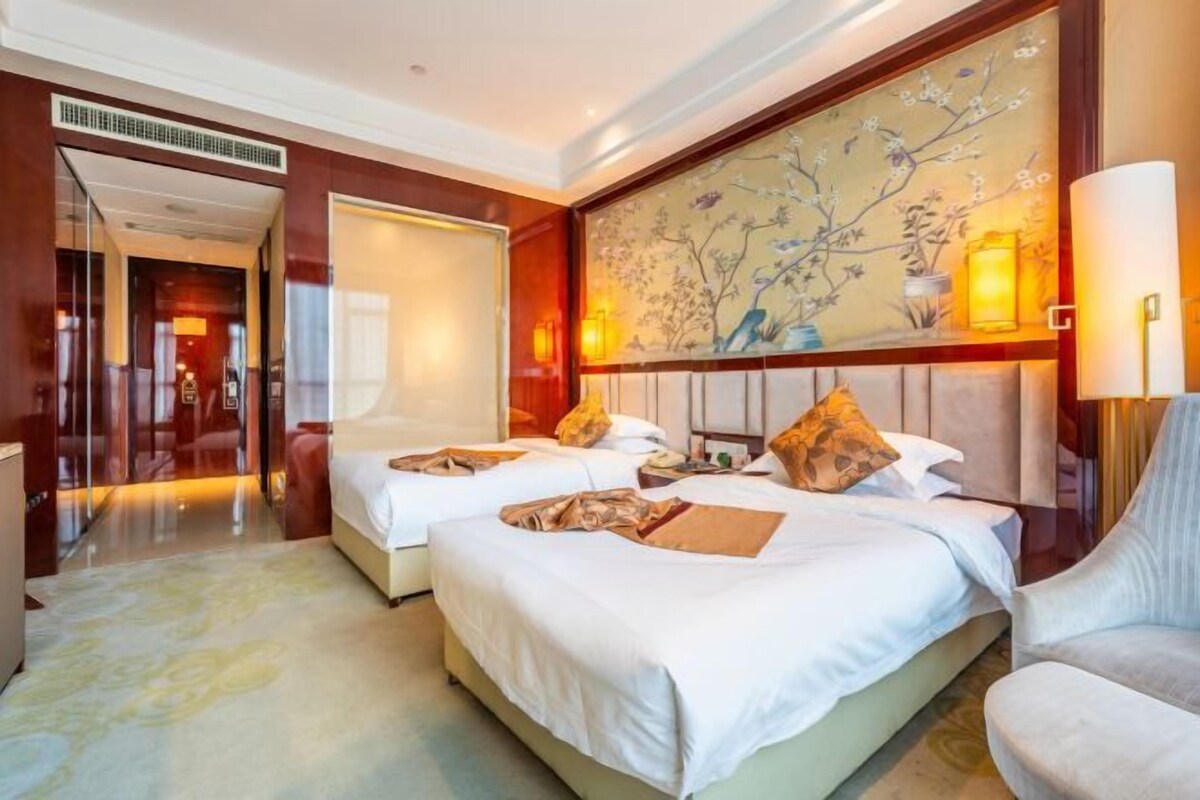 Une chambre d’hôtel avec deux lits, un grand tableau au mur et un coin salon avec un fauteuil.