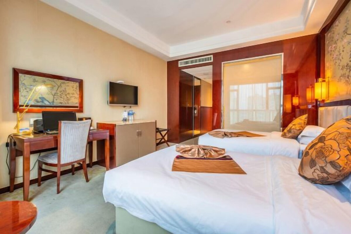 Une chambre d’hôtel avec deux lits, un bureau avec un ordinateur, une télévision et une armoire.