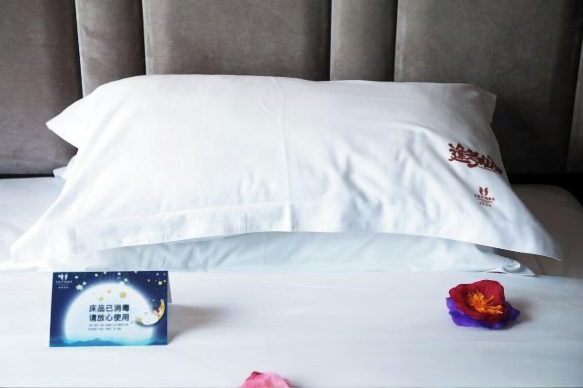 Un lit bien fait, avec un oreiller blanc et une petite carte posée à côté.