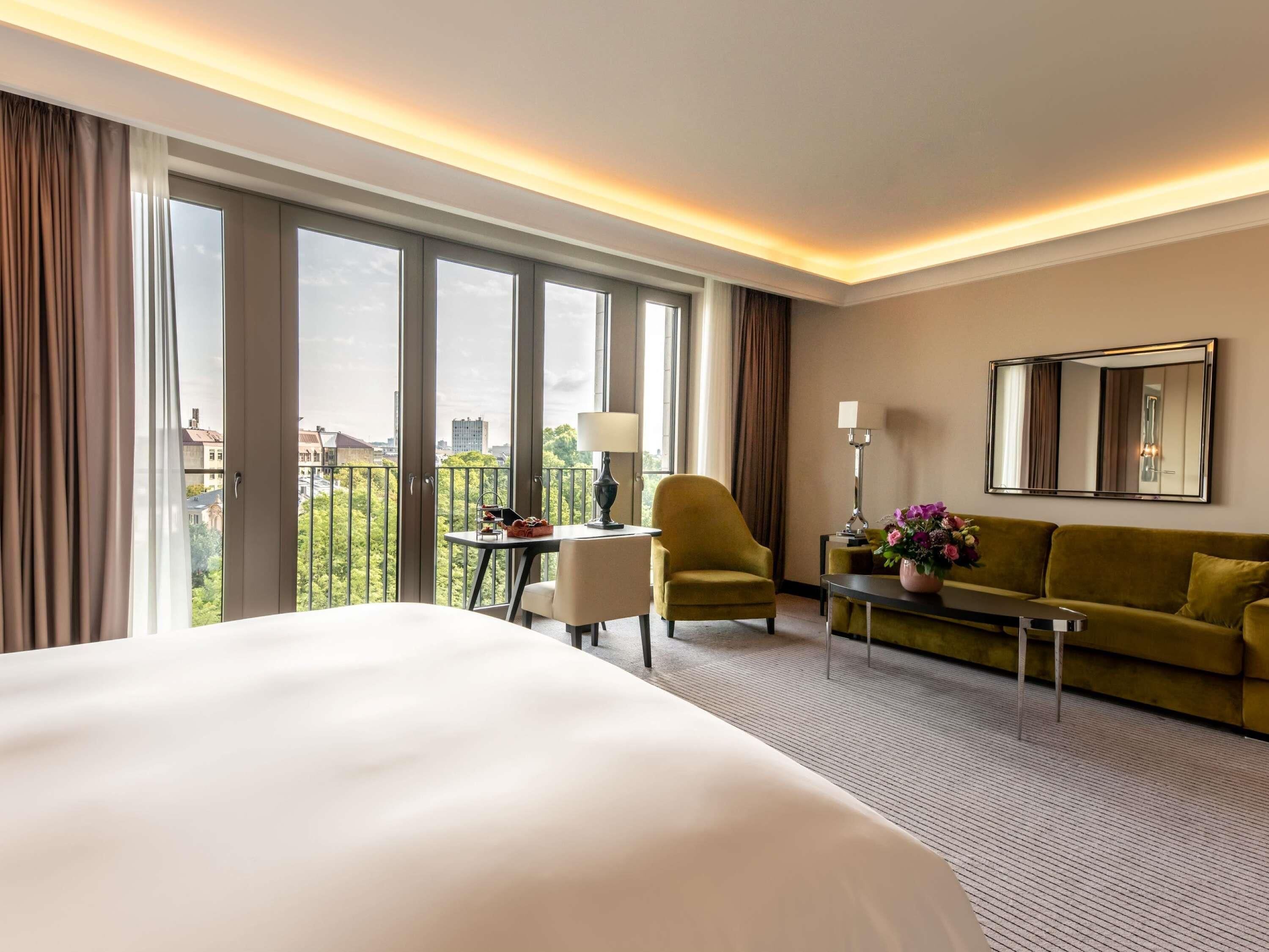 Habitación de hotel con una cama grande, un sofá, una silla, una mesita, una lámpara y un espejo en la pared.