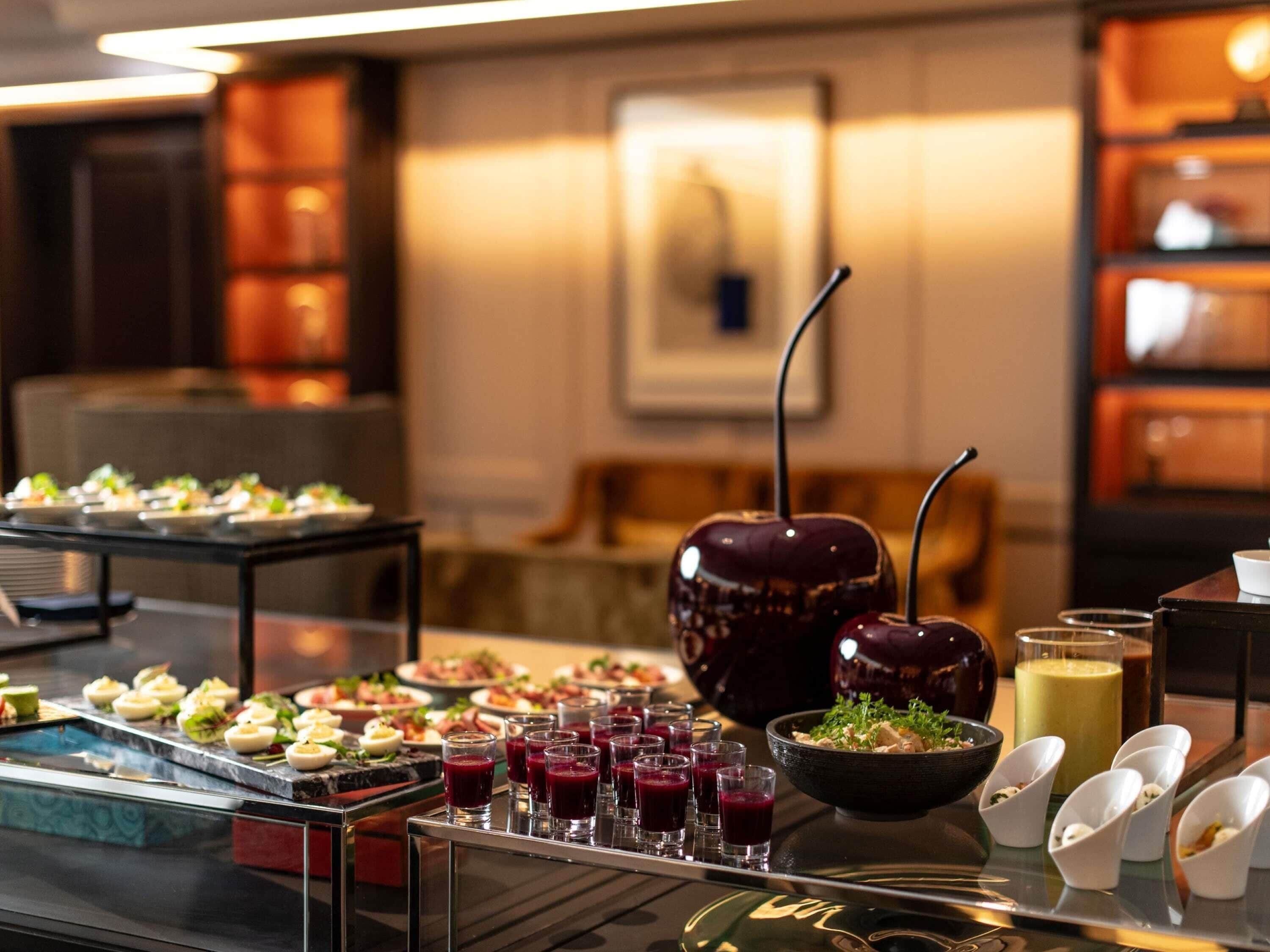 A buffet with various dishes and drinks, a large decorative vase, and a framed picture on the wall.