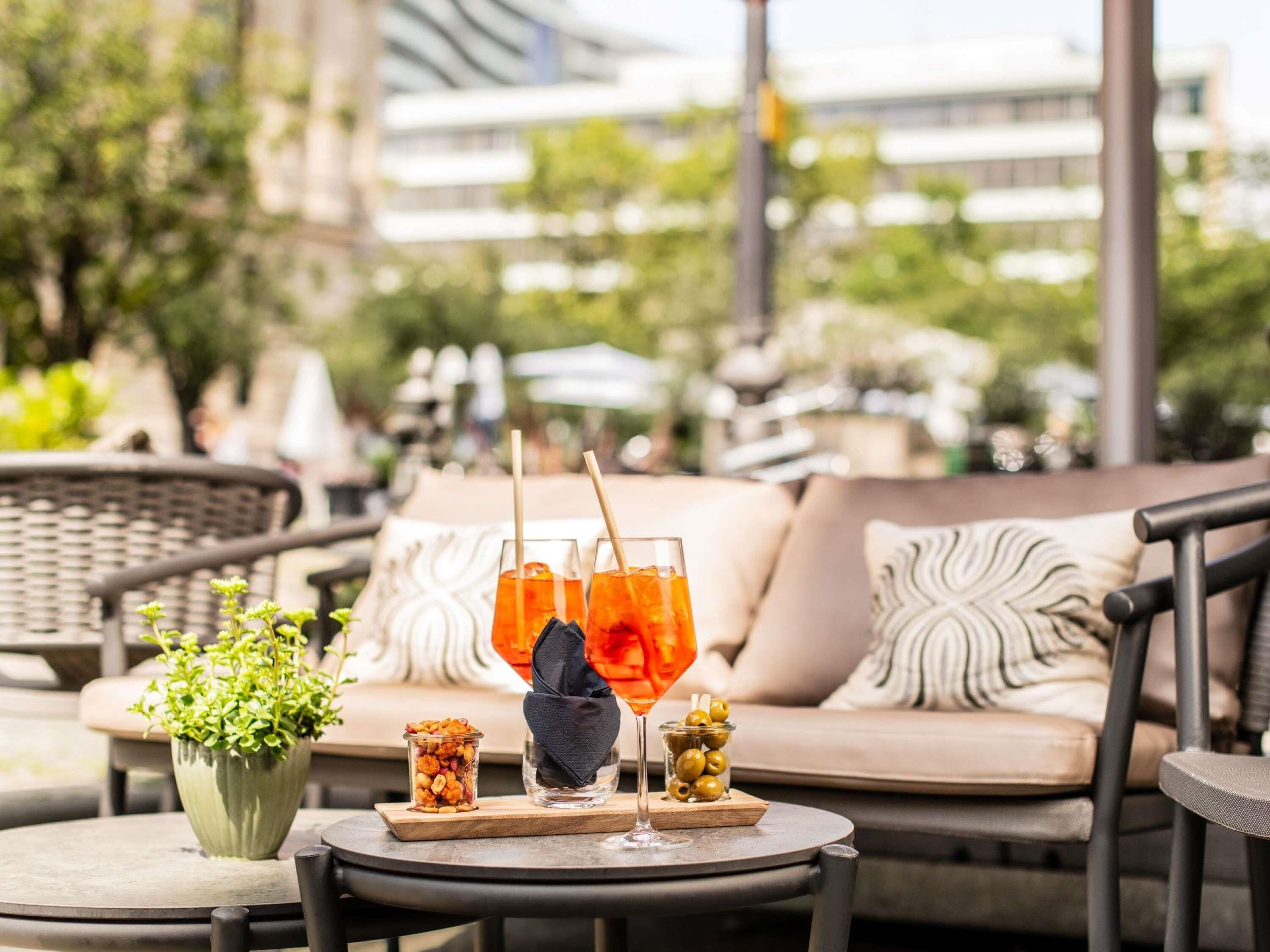 Una mesa con bebidas, aperitivos y una planta en maceta en un patio al aire libre.