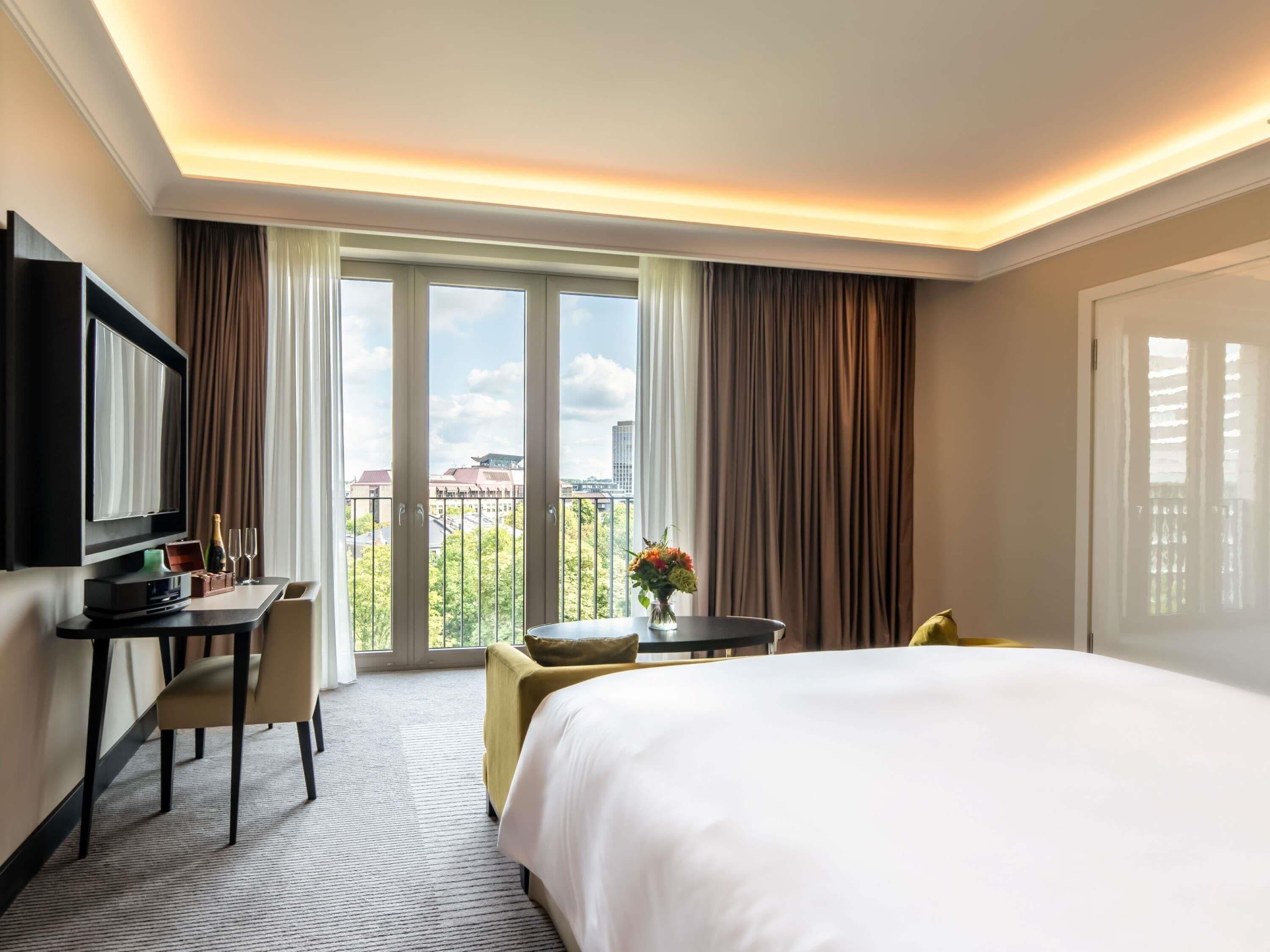 A hotel room with a bed, a desk, a TV, and a balcony with curtains.