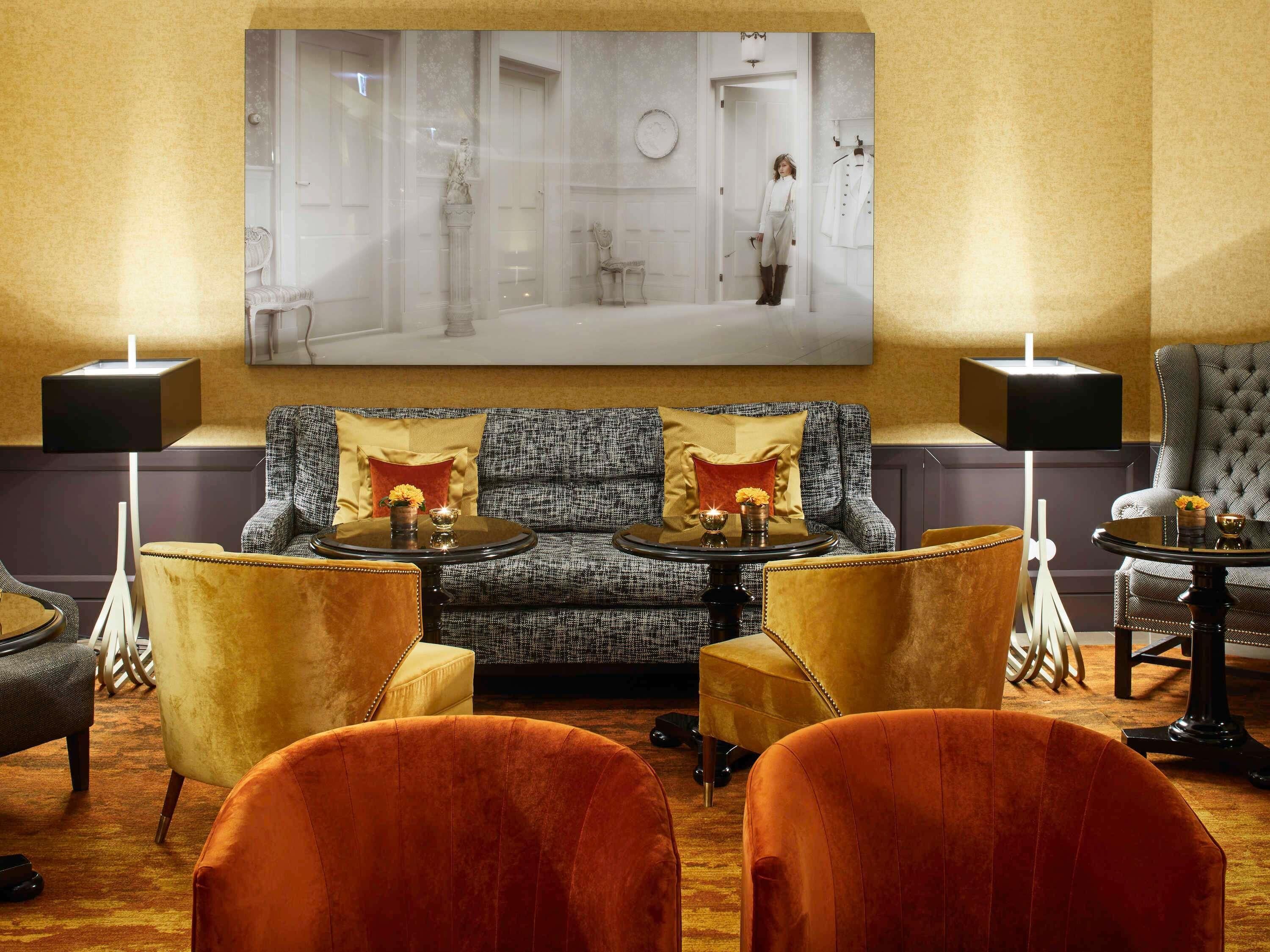 Eine Lobby mit einem grau gemusterten Sofa, zwei Sesseln, einem runden Tisch und einem großen gerahmten Bild an der Wand.