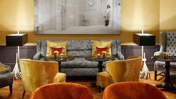 Eine Lobby mit einem grau gemusterten Sofa, zwei Sesseln, einem runden Tisch und einem großen gerahmten Bild an der Wand.
