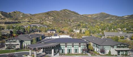 A modern hotel with a prominent sign, surrounded by a mountainous landscape and other residential buildings.