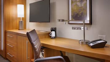 A hotel room with a wooden desk, a leather chair, a flat-screen TV, a coffee maker, a lamp, and a telephone.