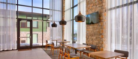 A spacious dining area with large windows, a brick wall, and modern pendant lights.
