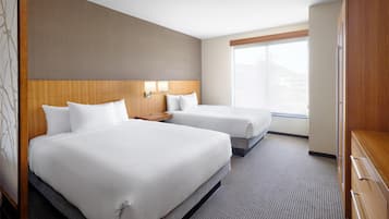 Habitación de hotel con dos camas, cabecero de madera, mesita de noche con lámpara, un ventanal grande y un armario.