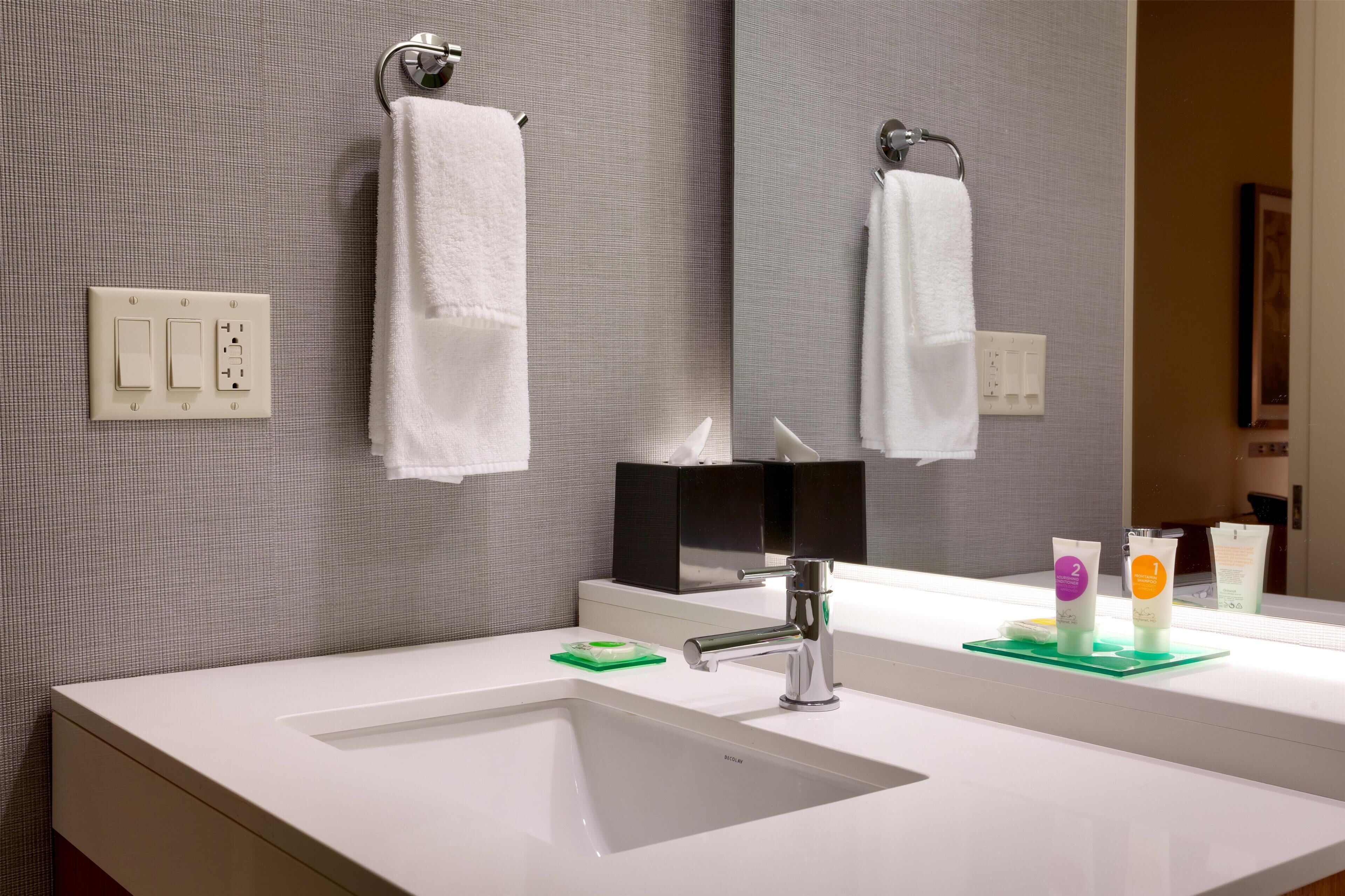 A bathroom with a white sink, a mirror, and two towels hanging on hooks.