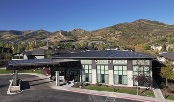 A modern building labeled "HYATT PLACE" with a covered parking area, surrounded by a mountainous landscape.