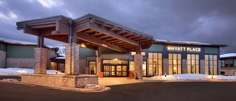 A Hyatt Place hotel with a covered entrance, stone pillars, and a snow-covered ground.