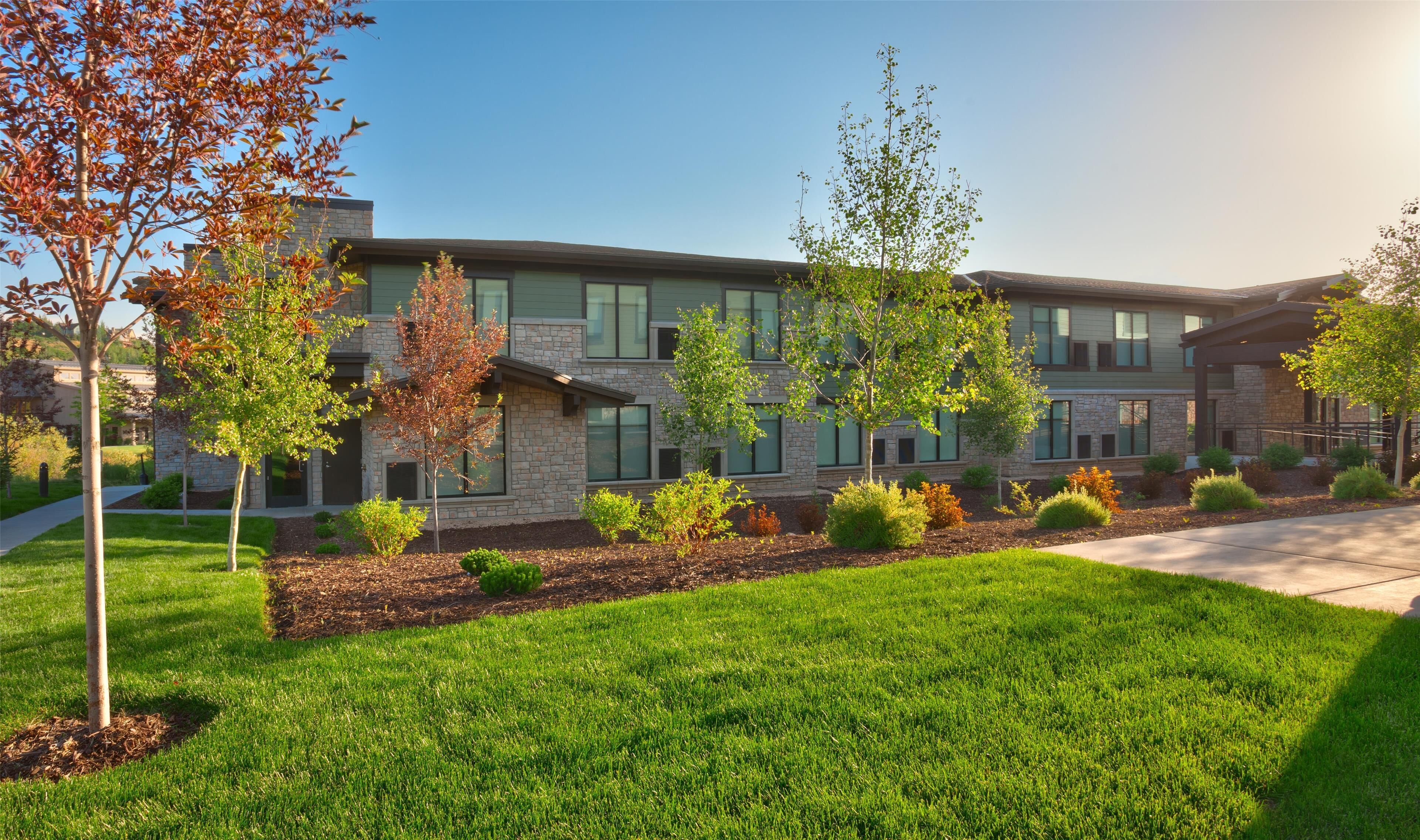 A modern building with a stone facade, large windows, and a well-maintained lawn with young trees.