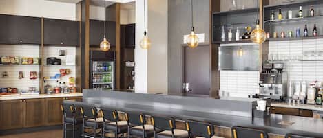 A modern kitchen with a bar area, featuring a long counter, bar stools, and hanging pendant lights.