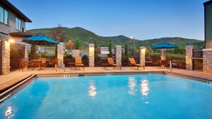 A swimming pool with lounge chairs and umbrellas, surrounded by stone walls and a view of hills. - Hyatt Place Park City (Park City)