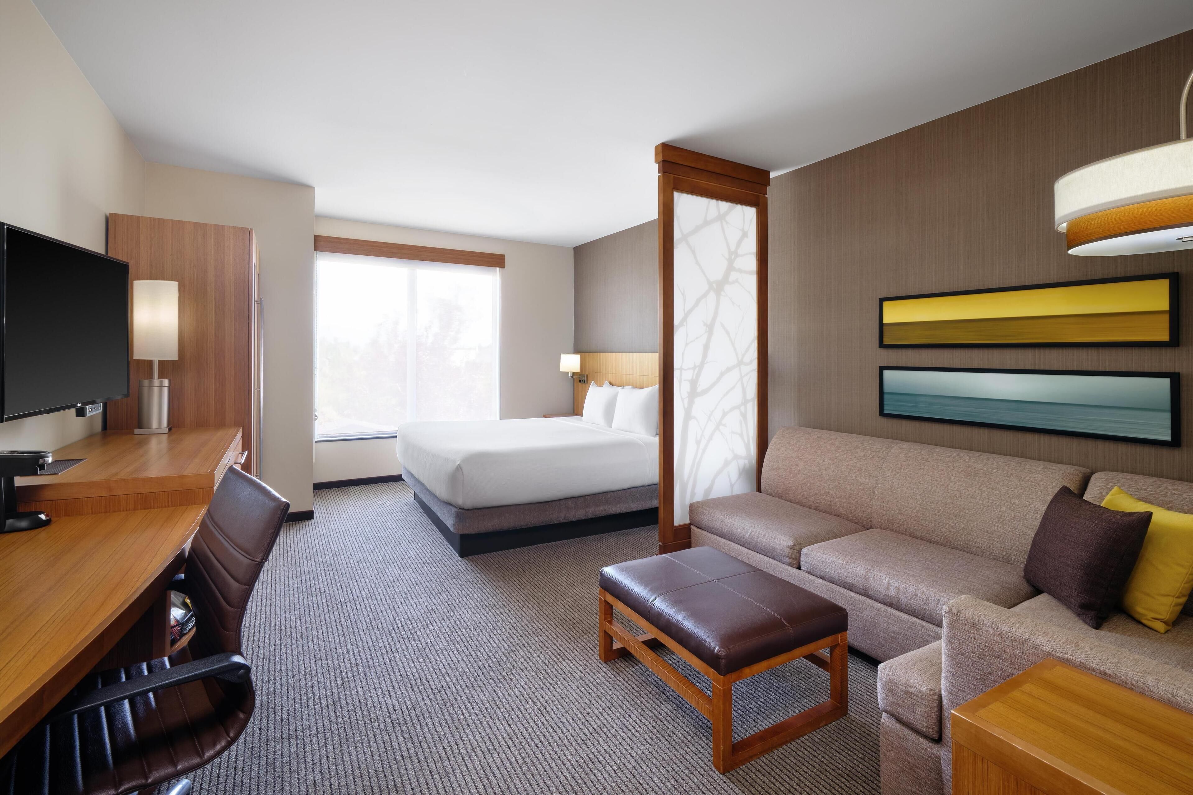 Habitación de hotel con cama, sofá, escritorio con silla, televisión y ventana.