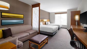 A hotel room with a sofa, two beds, a desk, a TV, and a large window.
