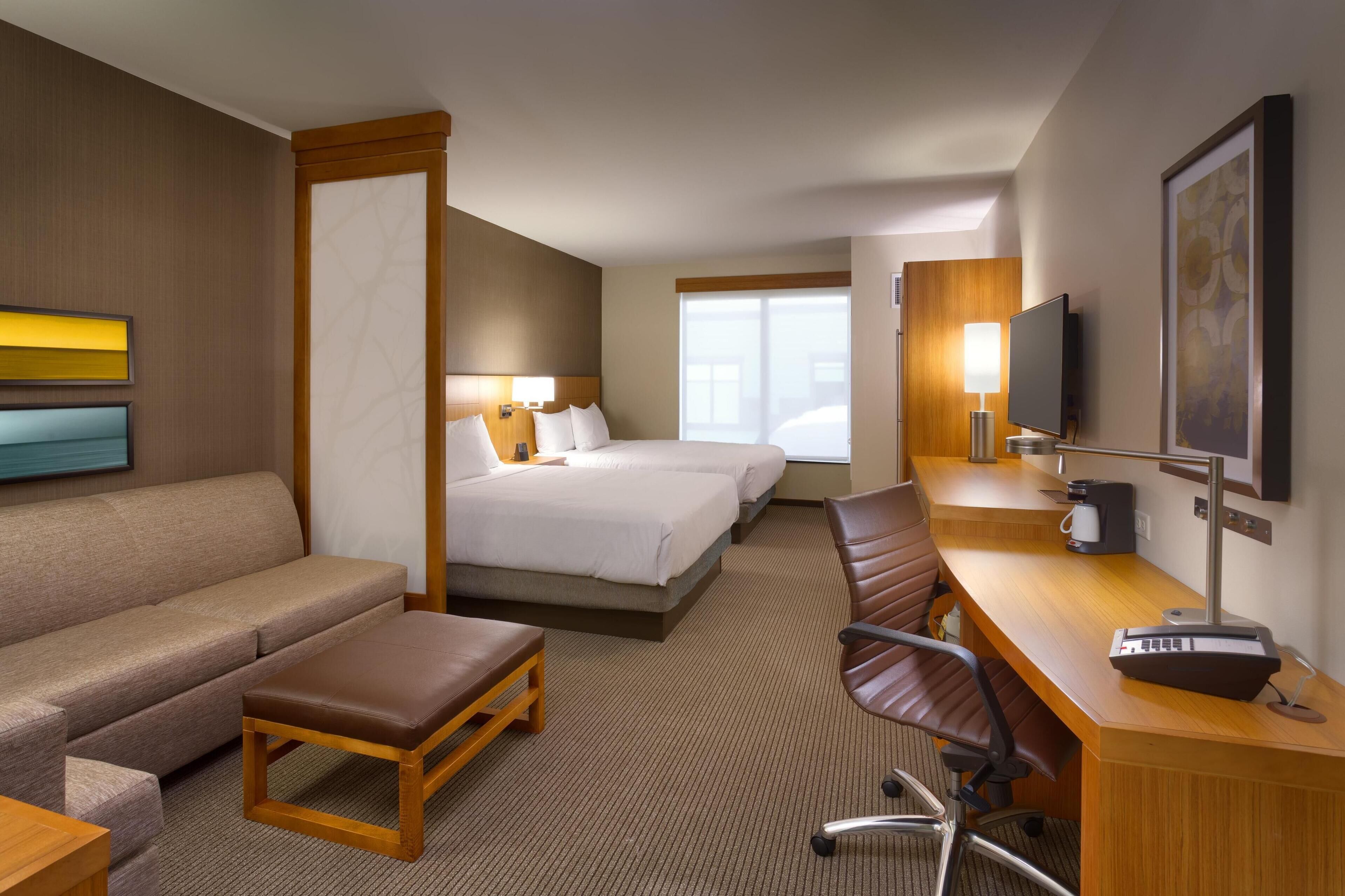 A hotel room with a bed, a sofa, a desk with a computer, a TV, and a window.