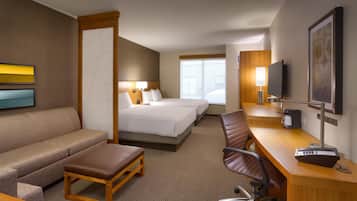 A hotel room with a bed, a sofa, a desk with a computer, a TV, and a window.