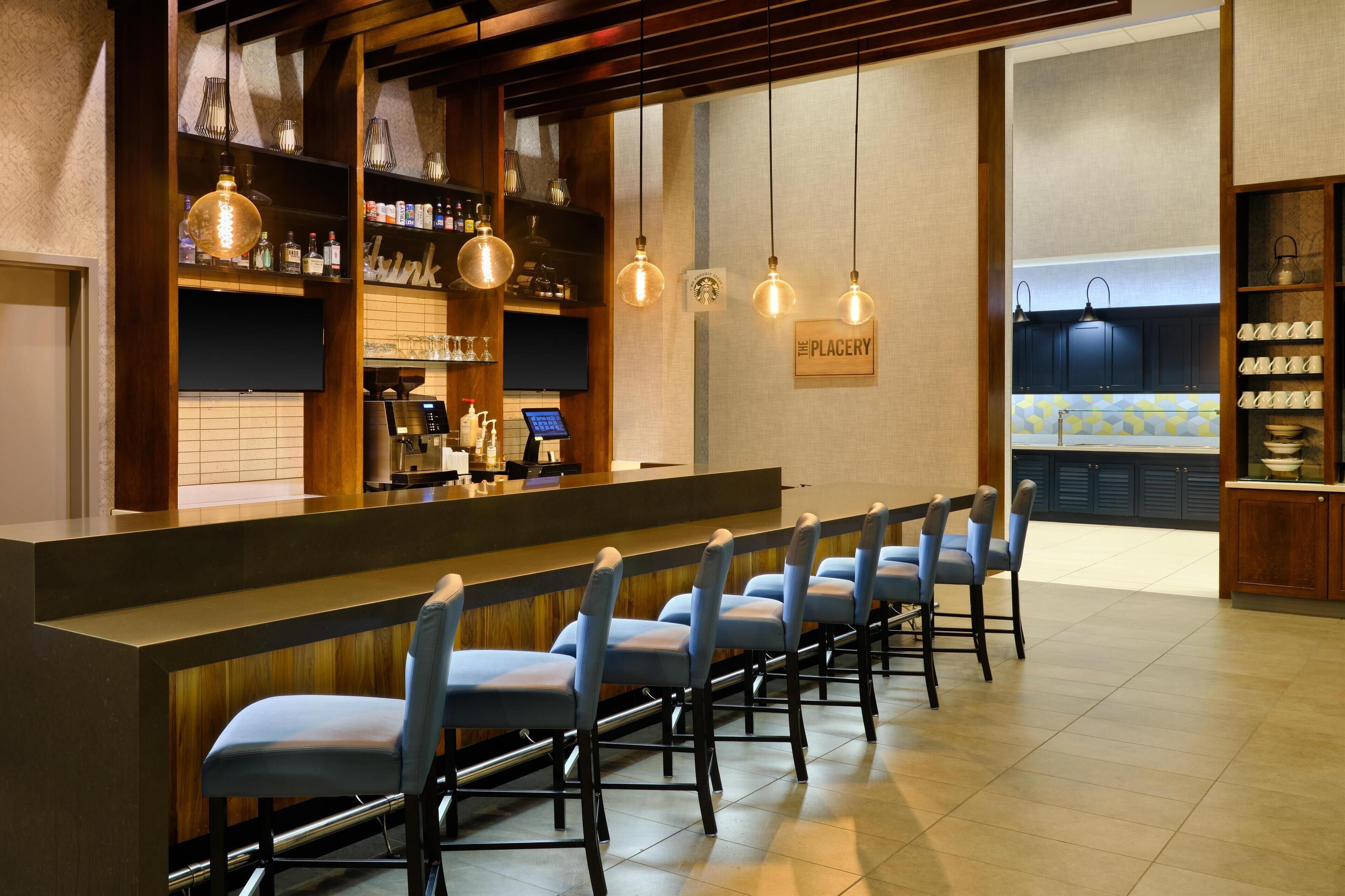 Un espace bar avec un comptoir, des tabourets de bar, des luminaires suspendus et une enseigne indiquant « PLACERY ».