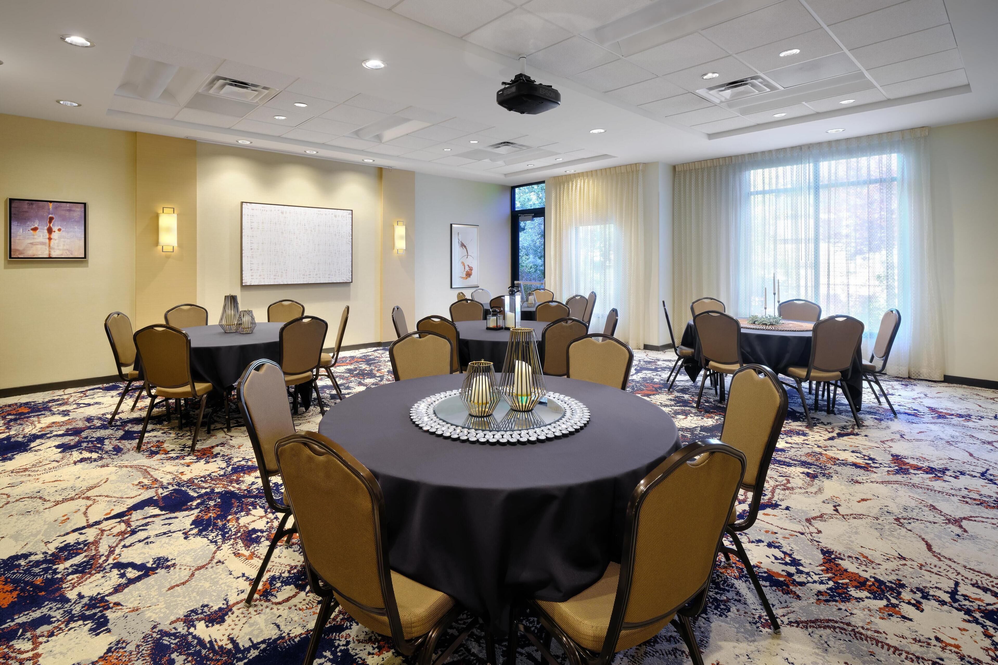 A conference room with round tables, beige chairs, a projector, and a whiteboard.