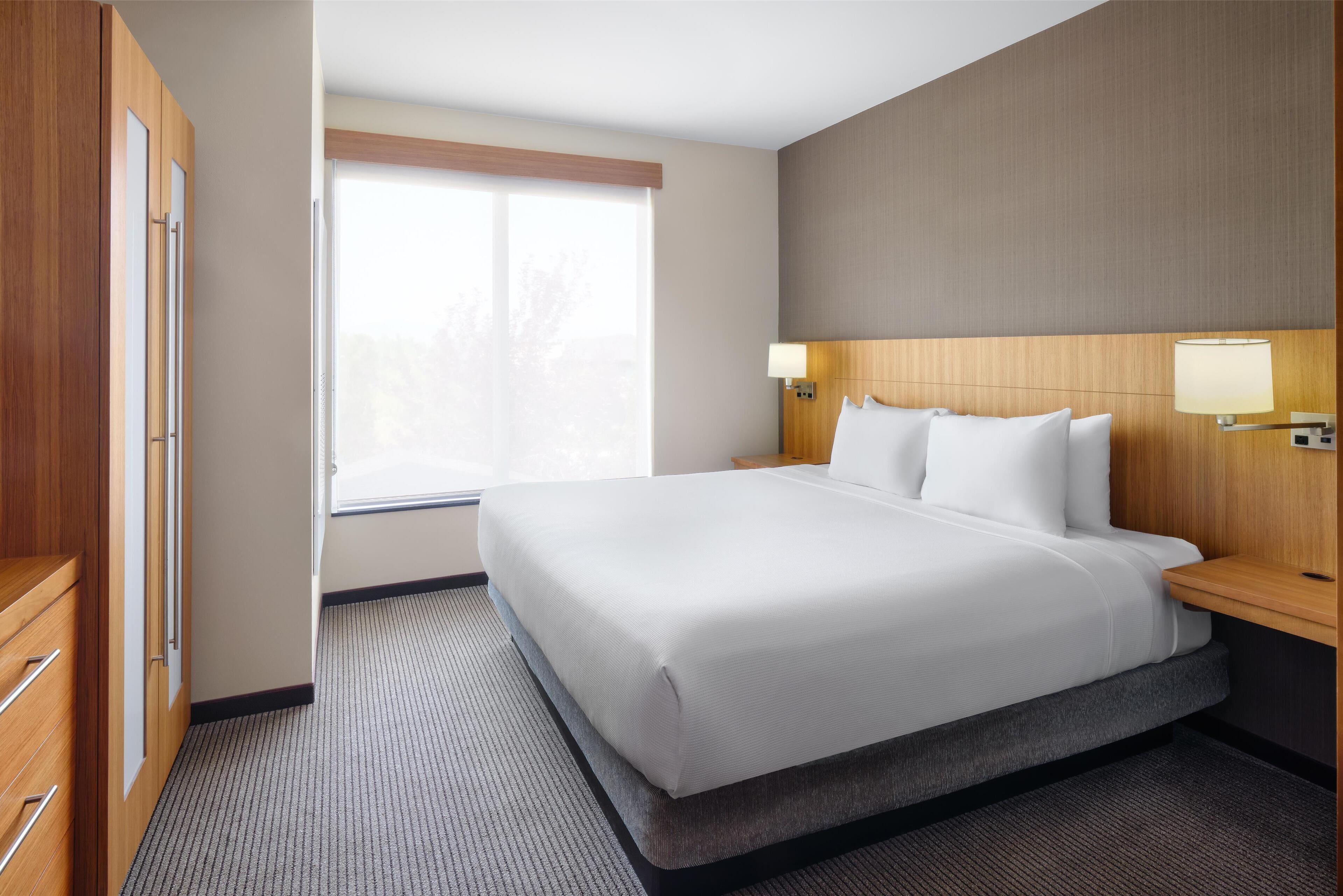 Une chambre d’hôtel avec un grand lit, une tête de lit en bois, des lampes de chevet et une fenêtre avec des stores.