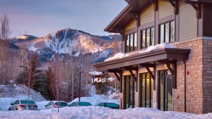 A modern building with a stone facade and large windows, surrounded by snow-covered ground and parked cars. - Hyatt Place Park City (Park City)