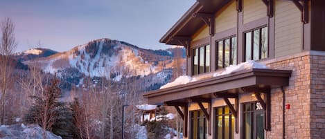 Un edificio moderno con fachada de piedra y ventanas amplias, rodeado de nieve y coches estacionados.