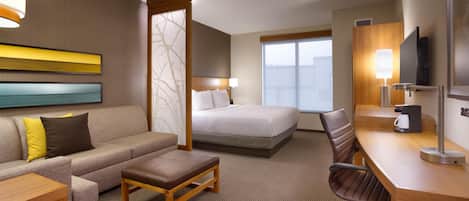 Habitación de hotel con cama, sofá, escritorio con silla, cafetera y televisión.