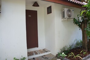A building entrance with a brown door, a small air conditioning unit mounted on the wall, and a tiled step leading to the door. - Vang Vieng Eco Lodge (Vang Vieng)
