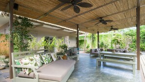 A covered outdoor seating area with a sofa and benches, surrounded by plants and a bamboo ceiling. - Tamarindo Bay Hotel & Apartments- Self Check In, Adults Only (Tamarindo)