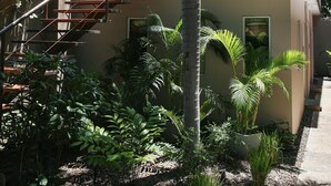A modern two-story building with a glass balcony, a staircase, and lush tropical plants. - Tamarindo Bay Hotel & Apartments- Self Check In, Adults Only (Tamarindo)