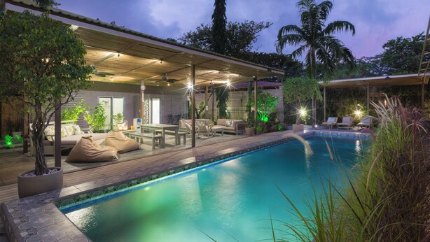 A pool area with a covered seating area, lounge chairs, and a small table. - Tamarindo Bay Hotel & Apartments- Self Check In, Adults Only (Tamarindo)