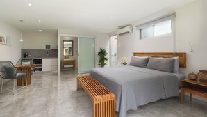 A modern bedroom with a large bed, a wooden bench, a desk, and a kitchenette. - Tamarindo Bay Hotel & Apartments- Self Check In, Adults Only (Tamarindo)