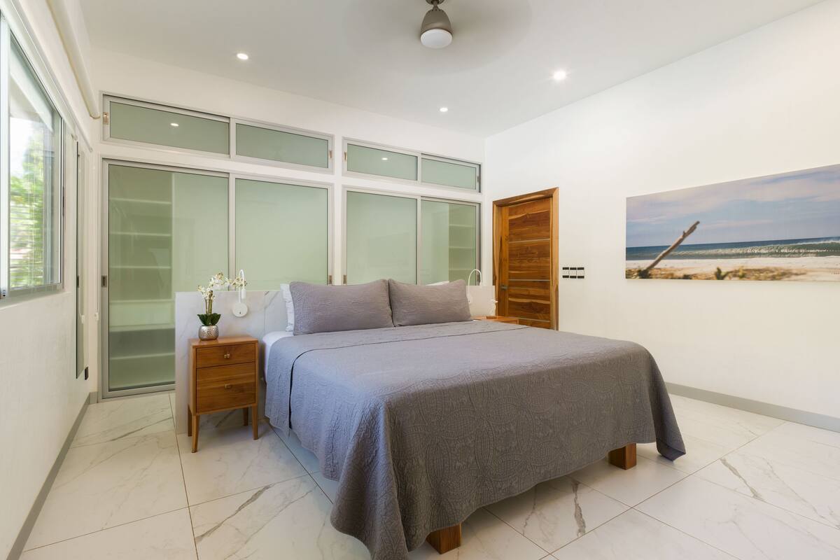 A bedroom with a bed, a nightstand, a window, and a painting on the wall.