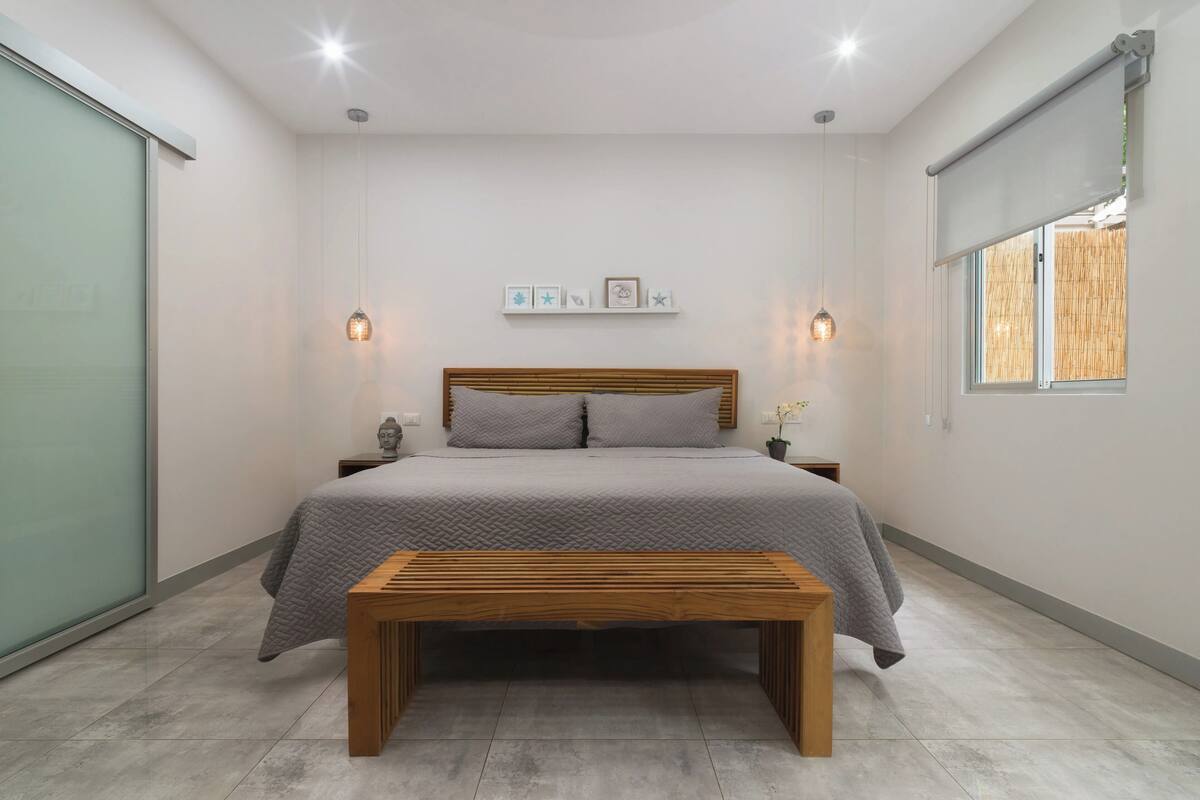A bedroom with a bed, bedside tables, a bench, and a window with a view.