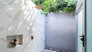 A modern bathroom with marble walls, a shower area, and a small shelf with flowers. - Tamarindo Bay Hotel & Apartments- Self Check In, Adults Only (Tamarindo)